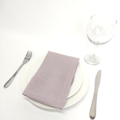 Conjunto de jantar com pratos brancos, guardanapo lilás, talheres metálicos e taça de vidro em mesa branca