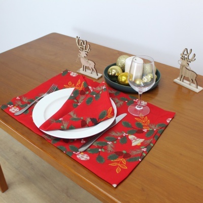 Mesa posta com individual e guardanapo vermelhos com padrão floral, prato branco, copo de vinho, talheres e decorações natalinas