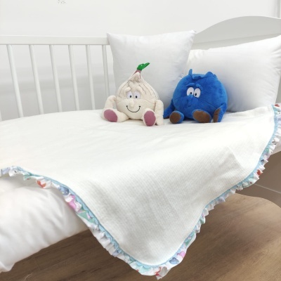 Cobertor branco com borda colorida floral sobre cama branca com dois peluches creme e azul