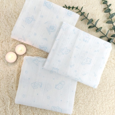 Três panos brancos com padrão azul claro, velas acesas e galho verde sobre superfície felpuda crema.