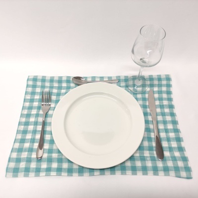 Mesa posta com guardanapo xadrez azul, prato branco, talheres metálicos e copo de vinho