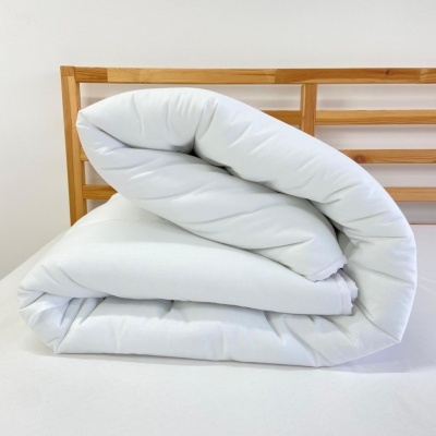 Colchão branco dobrado em cama com cabeceira de madeira clara