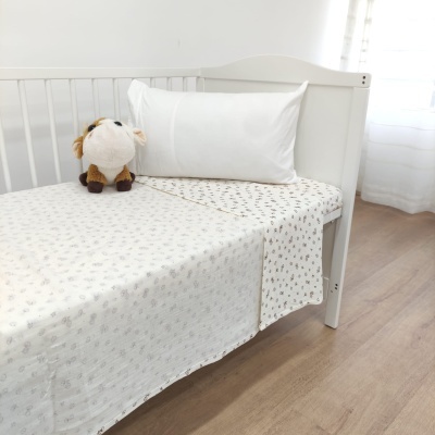 Berço branco com lençol padrão e peluche de vaca sobre colchão