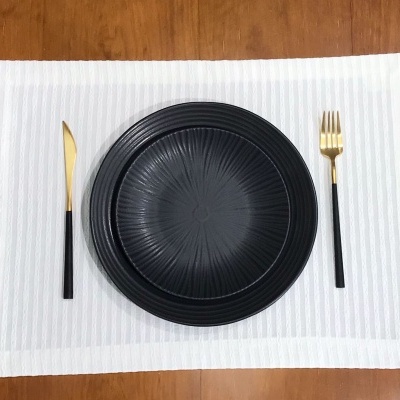 Talheres dourados e pretos com pratos pretos texturizados sobre pano branco em mesa de madeira