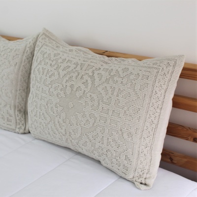 Travesseiro bege com textura bordada sobre cama branca com cabeceira de madeira