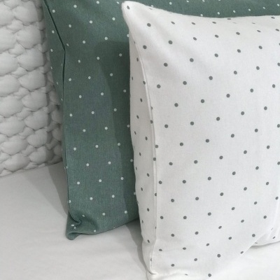 Almofadas verdes e brancas com padrão de bolinhas sobre superfície branca