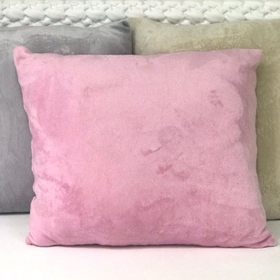 Três almofadas quadradas em tecido camurça cinza, rosa e bege diante de parede texturizada branca