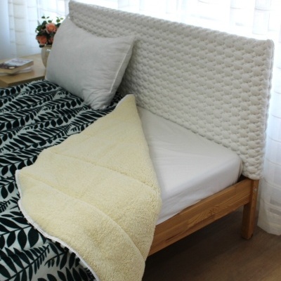 Cabeceira de cama branca texturizada com cama de madeira, almofada, edredão preto com folhas brancas e cobertor bege felpudo