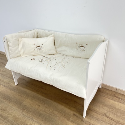 Berço branco de madeira com colcha acolchoada creme com desenhos infantis