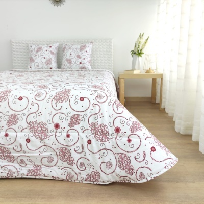 Colcha e almofadas com padrão floral vermelho e bege em quarto moderno com chão de madeira e decoração clara