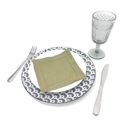 Conjunto de jantar com pratos decorados, guardanapo verde, talheres de aço inox e copo de vidro texturizado.