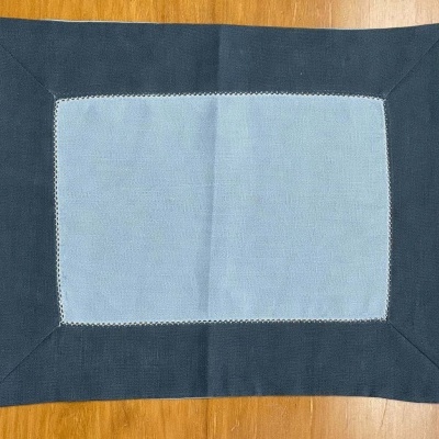 Toalha de mesa retangular azul claro com borda azul escuro sobre mesa de madeira.