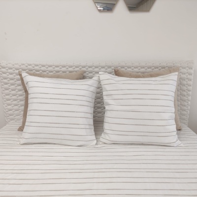 Cama com almofadas e lençol riscado branco e bege e cabeceira acolchoada branca