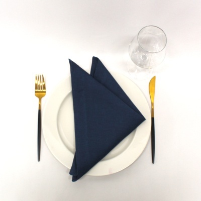 Conjunto de mesa com prato branco, guardanapo azul, talheres dourados e copo de vidro