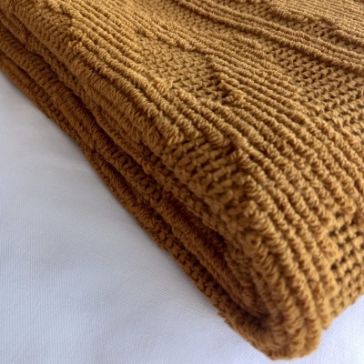Manta castanho-mostarda de lã ou algodão com textura canelada dobrada