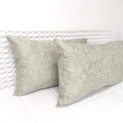 Almofadas retangulares decorativas com padrão paisley verde e bege sobre cama branca