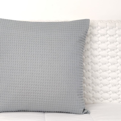 Almofada cinzenta texturizada sobre tecido branco com padrão em relevo