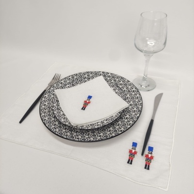 Conjunto de mesa com pratos decorados, guardanapo branco com soldado, talheres com cabos pretos e copo de vinho