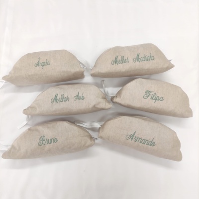 Seis almofadas pequenas de tecido bege com nomes bordados em verde claro