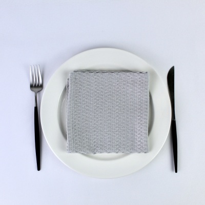 Prato branco com guardanapo cinzento, garfo e faca com cabo preto sobre mesa branca