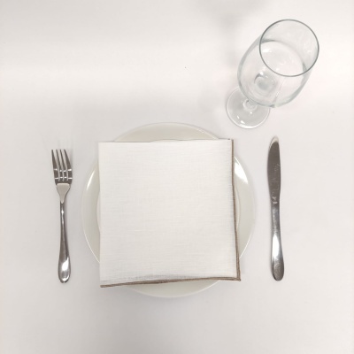 Mesa posta com prato branco, guardanapo, talheres de aço inoxidável e copo de vinho transparente