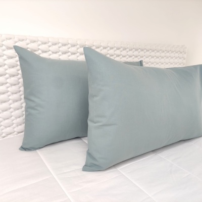 Três almofadas cinza-claro numa cama branca com cabeceira branca texturizada.