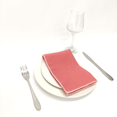 Conjunto de prato branco com guardanapo rosa, talheres de metal e copo de vinho