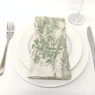 Guardanapo branco com padrão verde de folhas sobre prato branco com talheres e copo