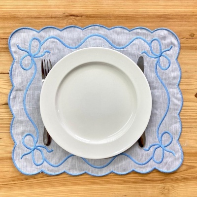 Jogo americano cinza com bordado azul e prato branco na mesa de madeira