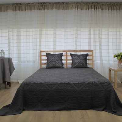 Quarto com cama de madeira coberta por colcha cinzenta e cortinas brancas ao fundo