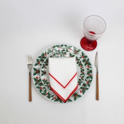 Conjunto de pratos decorados com folhas e bagas, guardanapo branco com borda vermelha, talheres com cabo de madeira e taça com base vermelha