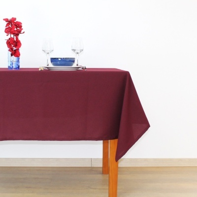 Mesa com toalha bordô, duas taças, prato branco com tigela azul e vaso azul com flores vermelhas