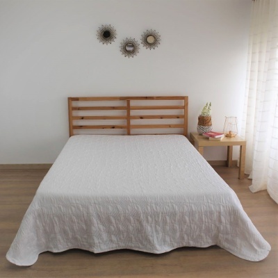 Cama de madeira clara com colcha branca, mesa de cabeceira com vaso e luminária e três espelhos redondos na parede