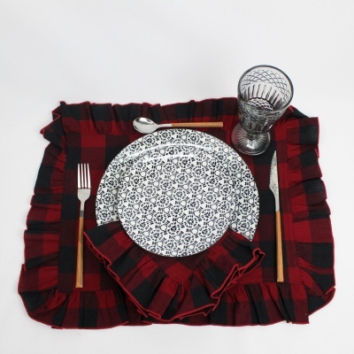 Jogo americano e guardanapo xadrez vermelhos e pretos com prato branco e azul, copo de vidro texturizado e talheres de cabo de madeira