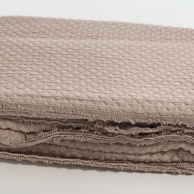 Manta bege com padrão em relevo dobrada sobre superfície branca