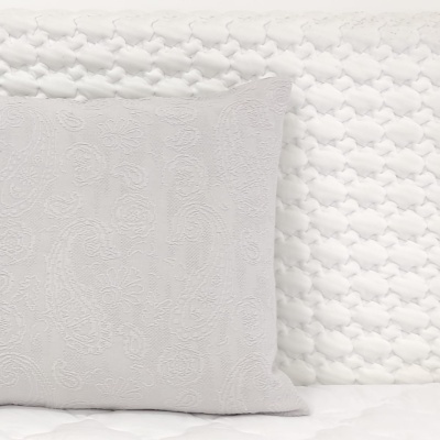 Travesseiro branco bordado sobre colchão acolchoado com padrão de losangos