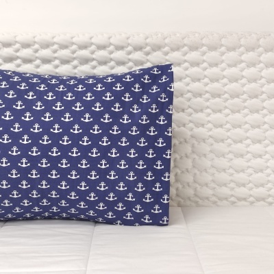 Travesseiro azul com âncoras brancas sobre colcha branca matelassada
