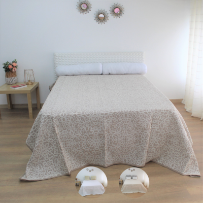 Cama de casal com colcha bege floral e cabeceira branca num quarto iluminado