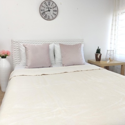 Cama arrumada com almofadas rosa e travesseiros brancos, relógio de parede e decoração minimalista