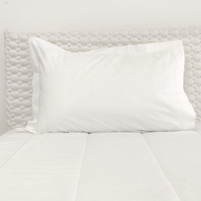 Travesseiro branco com fronha lisa numa cama com colchão e cabeceira texturizada