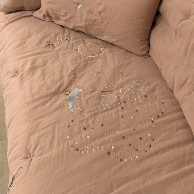 Capa de edredão castanha com desenhos bordados e a palavra Bella