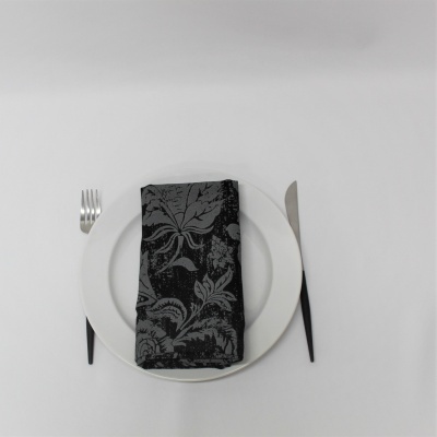 Prato branco com garfo e faca de cabo preto e guardanapo preto com padrão floral cinzento