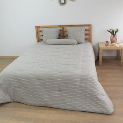 Cama com edredom cinza claro com padrão de pontos, almofadas e mesa de cabeceira com vaso de flores