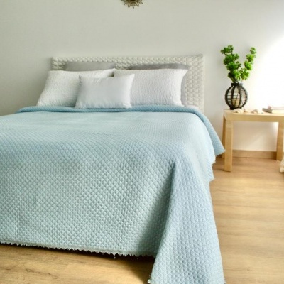 Cama com colcha azul clara e cabeceira branca ao lado de mesa com vaso e planta