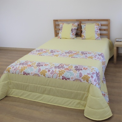Colcha verde clara com padrão floral e almofadas decorativas numa cama de madeira.
