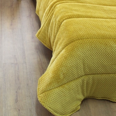Colcha amarelo mostarda com textura quadrada em cama sobre chão de madeira clara