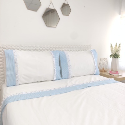 Roupa de cama branca com detalhes azuis e renda em quarto minimalista