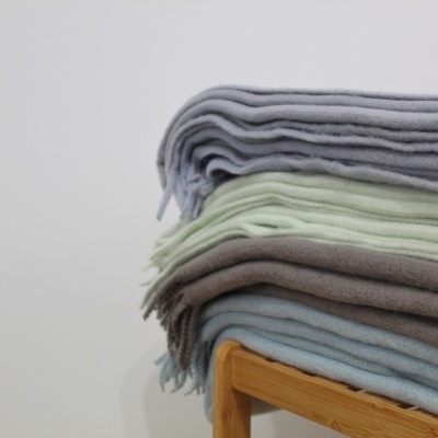 Mantas de lã empilhadas em cores cinza, verde claro, castanho e azul numa estrutura de madeira