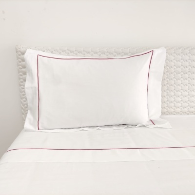 Travesseiro branco com linha vermelha fina em cima de lençóis brancos e colchão cinza texturizado