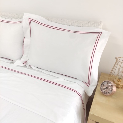 Jogo de cama branco com detalhes vermelhos num quarto minimalista com relógio cor de cobre na mesa de cabeceira